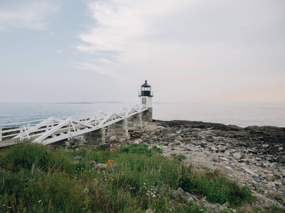 large white walkway connected to a white lighthouse that is sitting on rocks