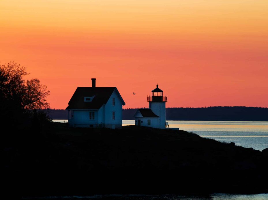 image of the sun rising behind a white lighthouse on an island